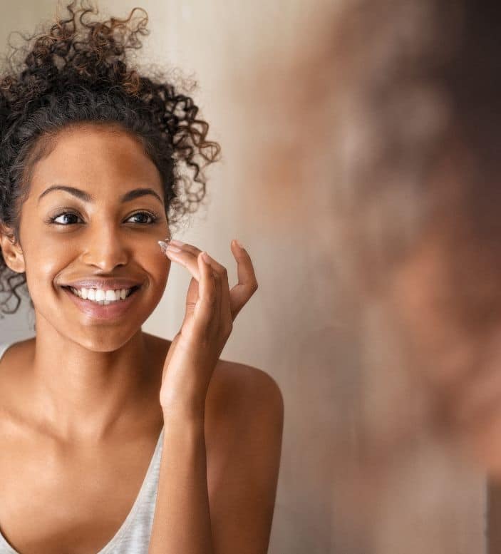 A woman looking in a mirror at clear skin after being treated by a dermatologist